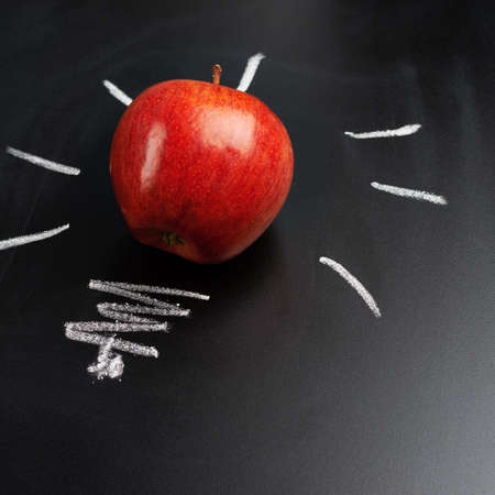 Red apple over the glowing bulb drawn on the blackboard as a back to school compositionの写真素材