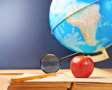 Studying geography composition of the red apple, old books, globe and magnifying glass against the...