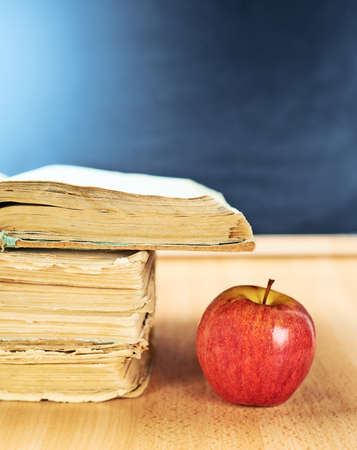 Red apple next to a pile of old books against the blackboard background as a back to school compositionの写真素材