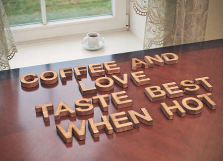 Coffee and love taste best when hot quote made with the block wooden letters over the table, next to a cup of coffee, composition with tone image correctionの写真素材