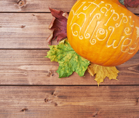 Pumpkin with the words Happy halloween carved over its surface over the colorful maple leaves and...