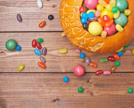 Halloween pumpkin with the words trick or treat carved over its surface and filled with multiple sweets and candies, composition over the wooden board backgroundの写真素材