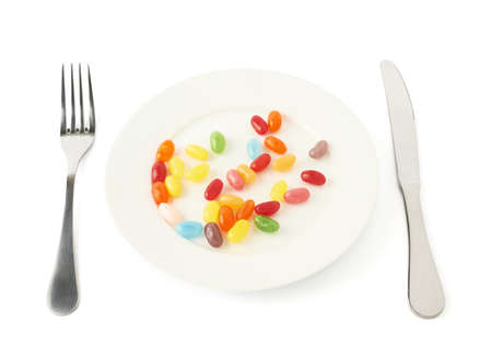 Multiple colorful candy beans in a white ceramic plate with the fork and knife next to it, composition isolated over the white backgroundの写真素材