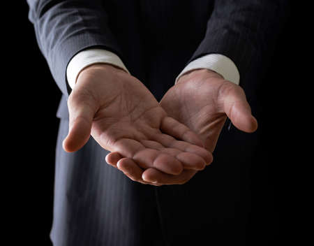 Two reaching out hands close-up shot of a caucasian man in a business suit, low-key dramatic light compositionの写真素材