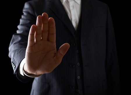 Open palm stop sign close-up shot of a caucasian man in a business suit, low-key dramatic light compositionの写真素材
