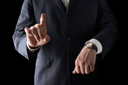 Pointing finger while showing time with the other hand close-up shot of a caucasian man in a business suit, low-key dramatic light compositionの写真素材
