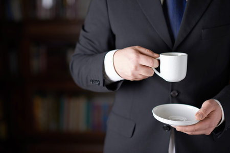 Close-up fragment of a man in a business suit holding a cup of coffee in front of him, shallow depth...
