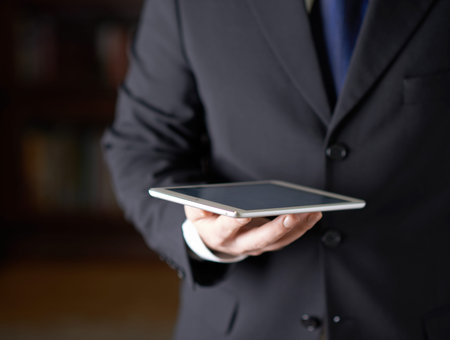Close-up fragment of a man in a business suit holding a pad tablet in his hands, shallow depth of...