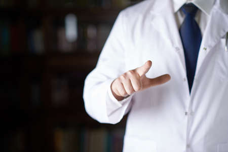 Close-up fragment of a man in a white doctors coat holding a pointing finger in front of him, shallow depth of field compositionの写真素材
