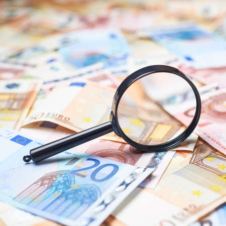 Magnifying glass over the surface covered with multiple euro bank note bills, shallow depth of field compositionの写真素材