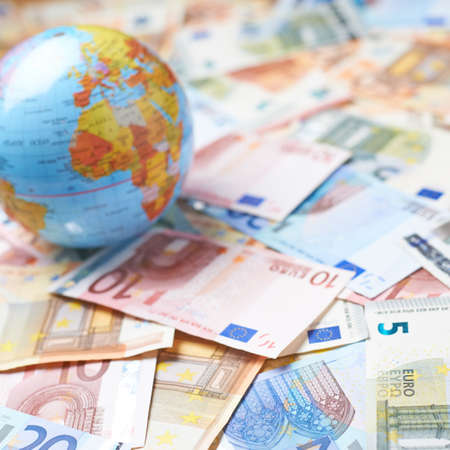Tiny Earth globe over the surface covered with the multiple bank note bills, shallow depth of field compositionの写真素材