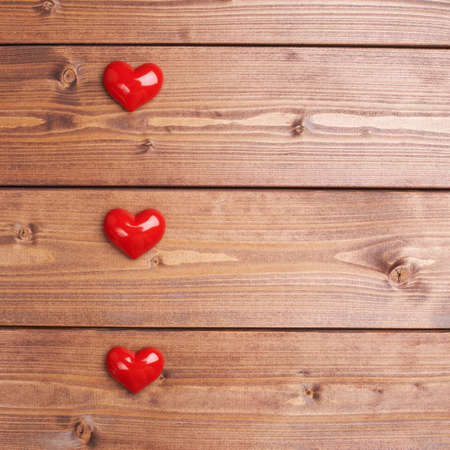 Three glossy red hearts over the brown wooden board surface as a love themed background compositionの写真素材