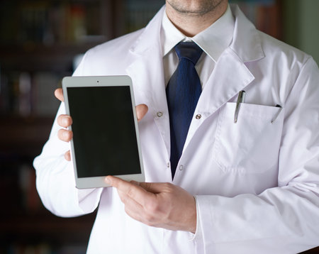Close-up fragment of a man in a white doctors coat holding a pad tablet device in his hands, shallow depth of field compositionの写真素材