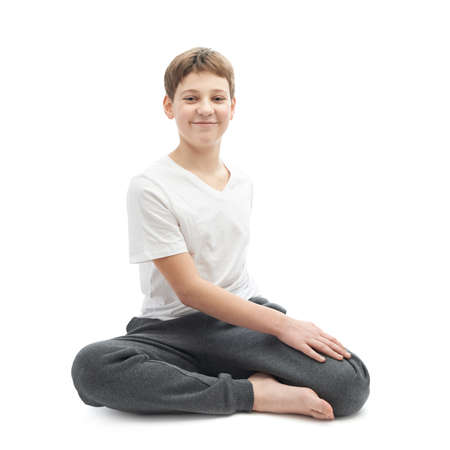 Caucasian 12 years old childen boy in a white t-shirt stretching or doing yoga. Composition isolated over the white backgroundの写真素材