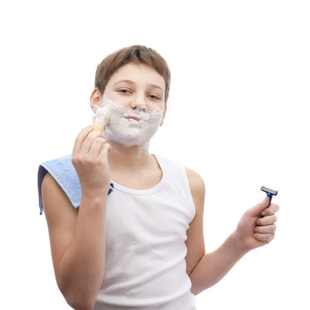 Happy young boy in a sleeveless white shirt with his face covered with the shaving foam, ready to shave, composition isolated over the white backgroundの写真素材