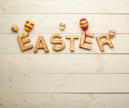 Word Easter made of wooden letters decorated with colorful toy eggs as a festive Easter background compositionの写真素材