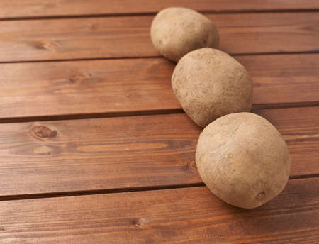 Three potatoes lying over the wooden tables surfaceの写真素材