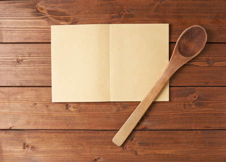 Composition of a wooden spoon next to copyspace empty recipe book over the wooden surfaceの写真素材