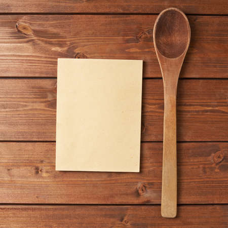 Composition of a wooden spoon next to copyspace empty recipe book over the wooden surfaceの写真素材