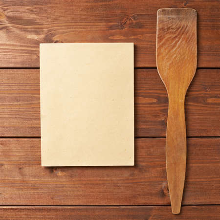 Composition of a wooden spatula next to the empty copyspace paper sheet over the wooden surfaceの写真素材