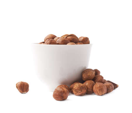 White ceramic cup bowl filled with the multiple hazelnuts isolated over the white backgroundの写真素材