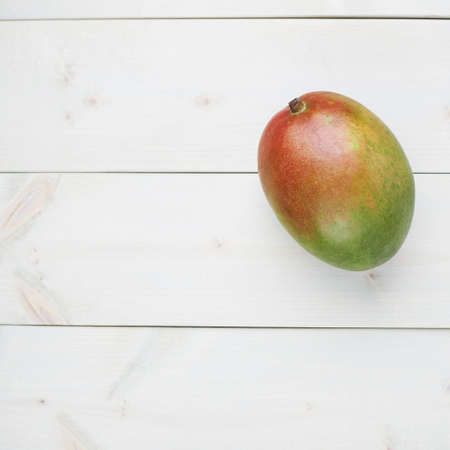 Ripe mango fruit lying over the white colored wooden board surface as a background compositionの写真素材