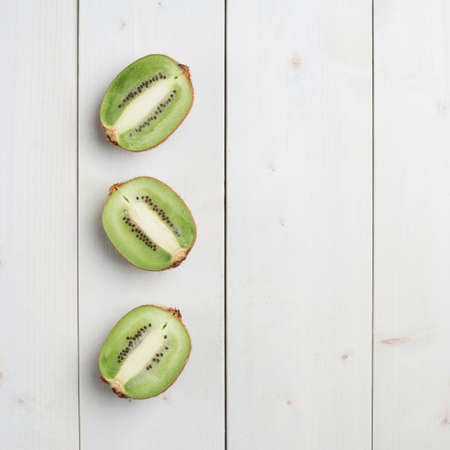 Three sliced halves of kiwi fruits or chinese gooseberry kiwi over the white wooden board surfaceの写真素材