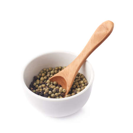 White ceramic bowl with the wooden spoon, filled with the mixed green and black peppercorn isolated over the white backgroundの写真素材