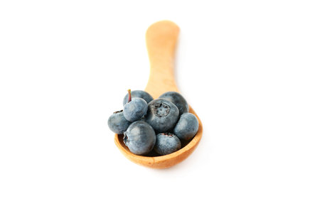 Wooden spoon filled of Ripe bilberry or blueberry over isolated white backgroundの写真素材