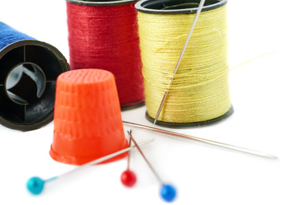 Spools of different threads, thimble and needles isolated over the white background, as sewing...