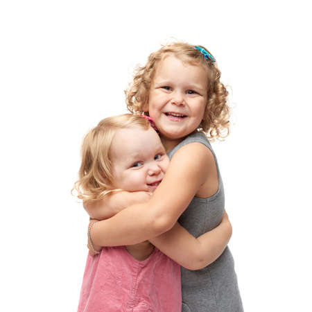 Couple of young little girls sisters with curly hair in gray and pink dress standing and cuddling over isolated white backgroundの写真素材