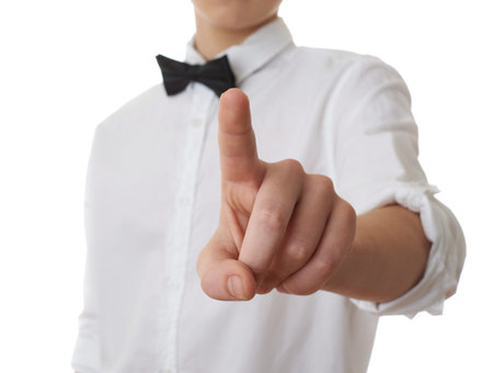 Cute teenager boy in white shirt and black bow tie pushing something in front himself over white...