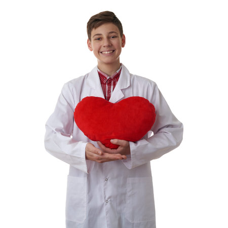 Cute teenager boy wearing white lab medic coat with red plush heart over white isolated background as science, medicine, healthcare conceptの写真素材