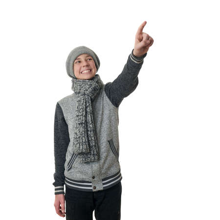 Cute teenager boy in gray sweater, hat and scarf pointing up over white isolated background, half bodyの写真素材
