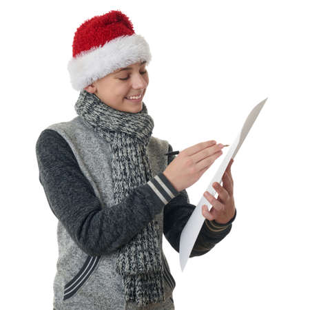 Cute teenager boy in gray sweater and christmas hat holding paper and pen over white isolated background, half bodyの写真素材