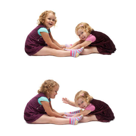 Couple of young little girls sisters with curly hair in purple dress sitting over isolated white backgroundの写真素材