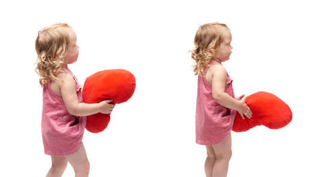 Young little girl with curly hair and red plush heart in pink dress standing over isolated white backgroundの写真素材