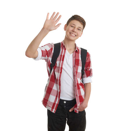 Cute teenager boy in red checkered shirt with school bag, waving hand over white isolated background, half body, as school, education conceptの写真素材
