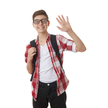 Cute teenager boy in red checkered shirt and glasses with school bag, waving hand over white isolated background, half body, as school, education conceptの写真素材