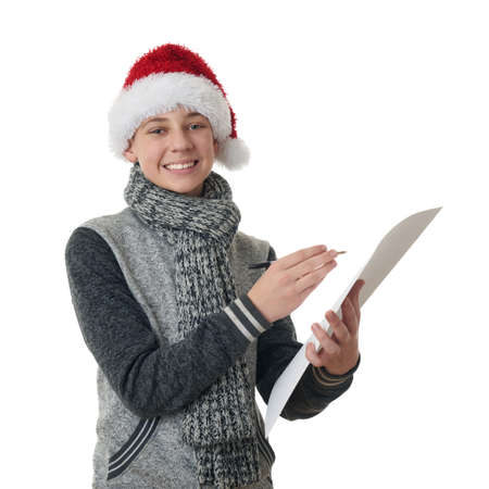 Cute teenager boy in gray sweater and christmas hat holding paper and pen over white isolated background, half bodyの写真素材