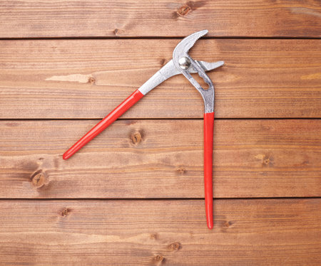 Metal plumber wrench with red handles on wooden brown surfaceの写真素材