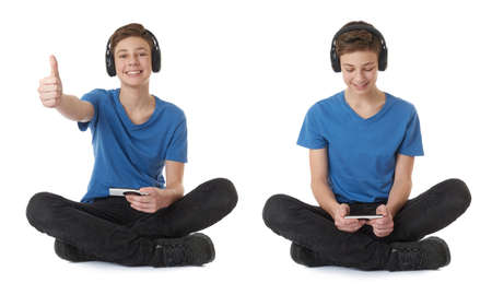 Cute teenager boy with smart phone in hands in blue T-shirt, headphones and lotus posture over white isolated backgroundの写真素材