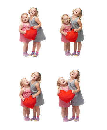 Couple of young little girls sisters with curly hair in gray and pink dress holding red plush heart and standing over isolated white backgroundの写真素材