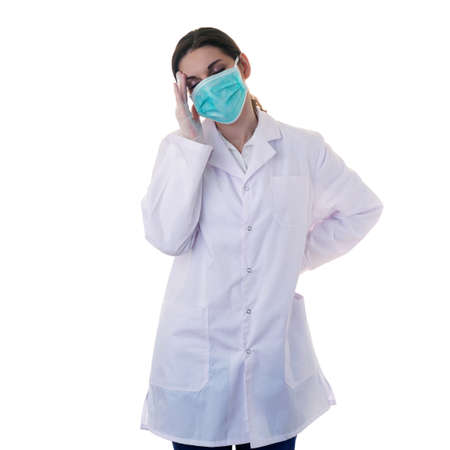 Female doctor in white coat over white isolated background in surgical mask touching head, healthcare, profession and medicine conceptの写真素材
