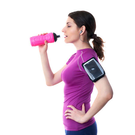 Smiling sporty woman in violet T-short with pink drinking bottle, smart phone device and headphones over white isolated background, fitness, sport and lifestyle conceptの写真素材