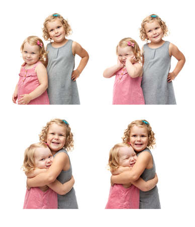 Couple of young little girls sisters with curly hair in gray and pink dress standing and cuddling over isolated white backgroundの写真素材