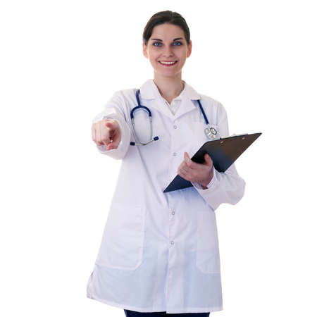 Smiling female doctor in white coat over white isolated background with stethoscope and clipboard pointing, showing direction or pushing button, healthcare, profession and medicine conceptの写真素材