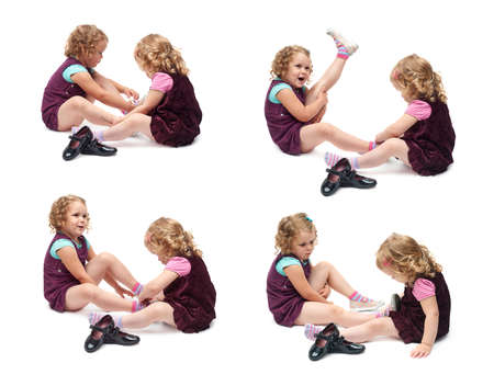Couple of young little girls sisters with curly hair in purple dress sitting and putting shoes over isolated white backgroundの写真素材