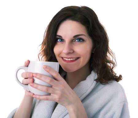 Smiling young woman in bath robe over white isolated background holding ceramic cup in hands, morning, healthy, relaxation and beauty conceptの写真素材
