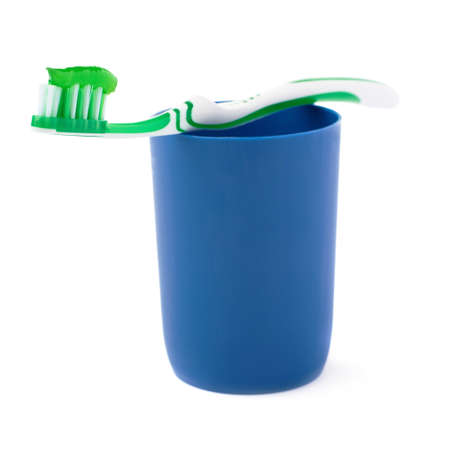 Green single toothbrush with paste lying on blue plastic cup isolated over white backgroundの写真素材